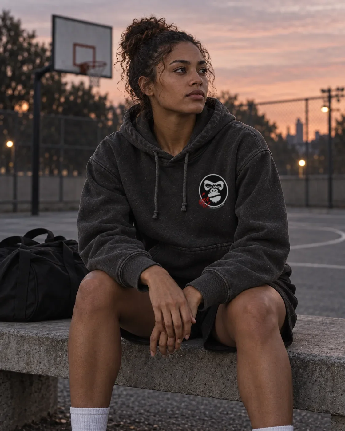 Illustrative campaign: an adult athlete in the charcoal GC Hoodie resting alone courtside at dusk